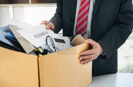 Homme d'affaires transportant l'emballage de tous ses effets personnels et dossiers dans une boîte en carton marron pour démissionner dans un bureau moderne, démissionner concept.