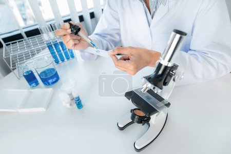 Photo for Scientist woman holding dropper to dropping solution sample on the glass plate for microscope to research and experiment about coronavirus vaccine while working in laboratory - Royalty Free Image