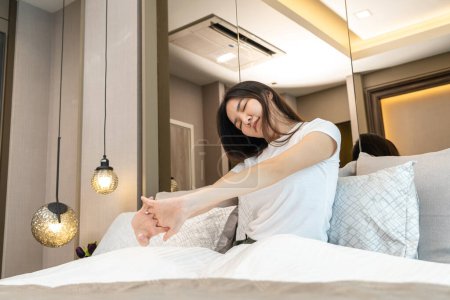 Photo for Asian woman is smiling and raising arms to stretching on the bed in bedroom with feeling refreshed and relaxed after wake up in the morning - Royalty Free Image