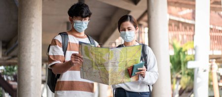 Photo for Tourist couple with luggage looking on the map to searching direction destination for honeymoon trip while wearing medical face mask to protection from coronavirus and travel with new normal lifestyle - Royalty Free Image