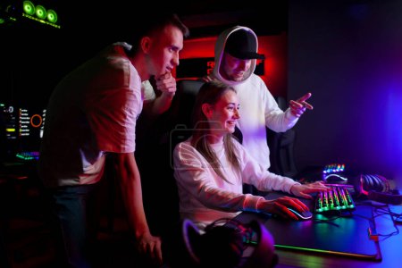 young guys gamers teach a girl to play a computer game look at the monitor and communicate, a company of young people in a computer club