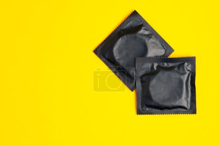 Téléchargez les photos : Two black condom on yellow background, top view, safe sex concept - en image libre de droit