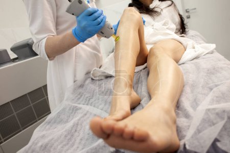 leg epilation procedure in cosmetology clinic, cosmetologist doctor makes depilation of girl with alexandrite laser, hair removal with modern equipment