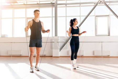 Téléchargez les photos : Jeune couple athlétique en entraînement corde à sauter dans la salle de gym le matin, homme entraîneur et femme aller dans le sport, mode de vie sain - en image libre de droit