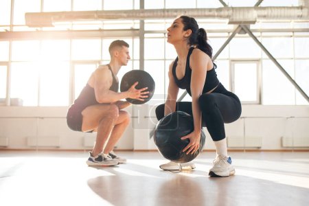 Photo for Young beautiful athletic couple in sportswear at crossfit training with ball in the fitness room, woman and man together at fitness training go in for sports and do endurance exercise - Royalty Free Image