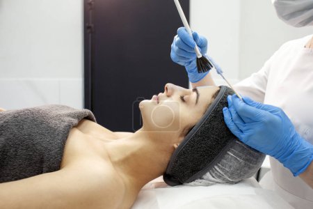 cuidado profesional de la piel en la clínica de cosmetología, dermatólogo médico aplica crema con cepillo en la cara del paciente femenino, procedimiento de descamación de la piel facial