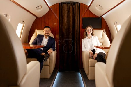 Geschäftsleute sitzen im Privatjet und fliegen im Flugzeug, erfolgreiche asiatische Geschäftsleute mit Kollegin fliegen First Class