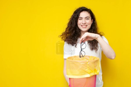 Photo for Young cheerful girl throws glasses into trash can, the concept of treatment and vision correction, woman with good eyesight refuses glasses, copy space - Royalty Free Image