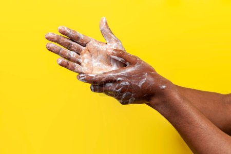 Photo for African american man washes his hands with soap on yellow isolated background, hands in cream and foam, close-up - Royalty Free Image