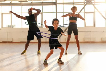 Photo for Sporty african american family in sports uniform twists hula hoop and does exercises in the gym, boy with his parents goes in for sports and trains - Royalty Free Image