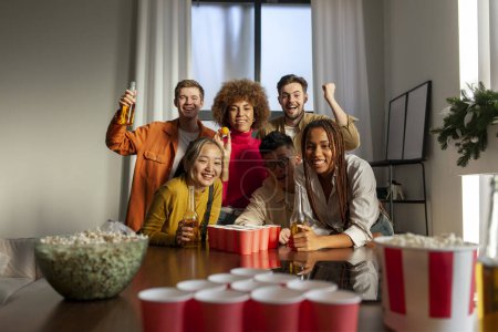 Téléchargez les photos : Groupe multiracial de jeunes amis jouant au bière-pong lors d'une fête boire de la bière et s'amuser à la maison, étudiants buvant de l'alcool et célébrant la victoire - en image libre de droit