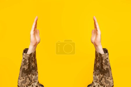 manos de soldado ucraniano en camuflaje píxel uniforme militar levantado sosteniendo y mostrando espacio vacío sobre fondo aislado amarillo, manos militares vacías publicidad espacio de copia
