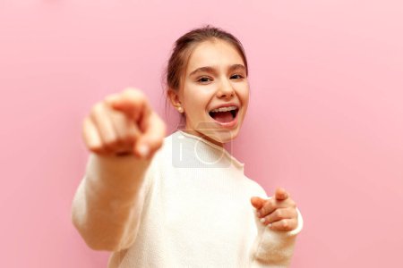 Ich wähle dich. fröhliches Teenagermädchen mit Zahnspange zeigt mit den Händen nach vorne und spottet über einen rosafarbenen isolierten Hintergrund, das Kind scherzt und spottet und wählt dich