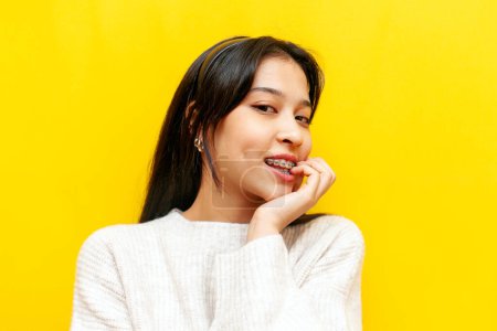 Téléchargez les photos : Jeune fille asiatique coûteuse avec bretelles flirte et pense sexuellement sur fond jaune isolé, excitée fille coréenne rêve et imagine et mordu un doigt - en image libre de droit