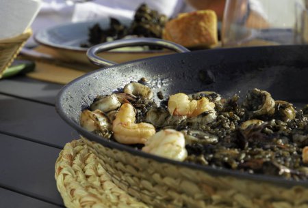 Photo for Black rice with squid and shrimps in a paella pan. Ready to eat, with bread and red wine - Royalty Free Image