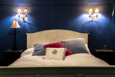 Ein Bett mit weißem Kopfteil und Kissen und eine Lampe auf dem Nachttisch. Der Raum ist blau-weiß dekoriert, was ihm eine ruhige und ruhige Atmosphäre verleiht
