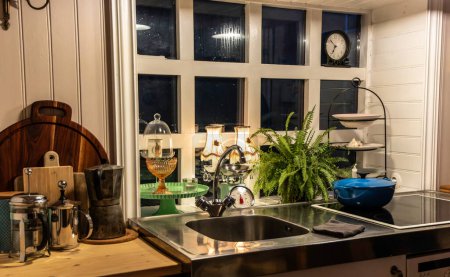 Eine Küche mit Fenster und Uhr an der Wand. Die Küche ist gut beleuchtet und hat eine gemütliche Atmosphäre