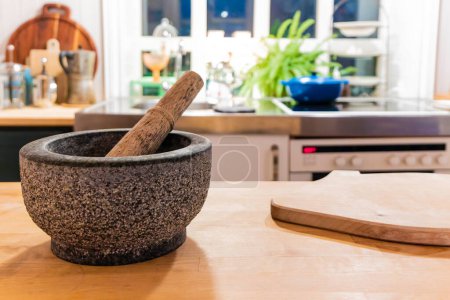 Ein Schneidebrett aus Holz steht auf einer Theke neben Mörser und Stößel. Die Küche ist hell und sauber, mit einer Topfpflanze im Hintergrund. Konzept von Ruhe und Ordnung