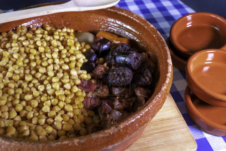 A bowl of food with chickpeas and other ingredients. The bowl is on a wooden table. There are three other bowls on the table. Typical spanish cocido