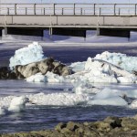 A bridge over a body of water with ice floating on top. The ice is large and scattered throughout the water