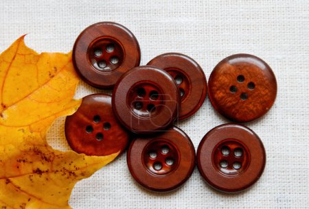 Seven brown buttons and yellow maple leaf on a white textile background