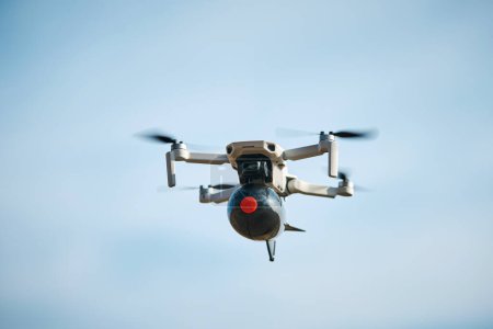 Téléchargez les photos : Drone civil grand public avec une grosse bombe en plastique à bord vole dans le ciel bleu - en image libre de droit