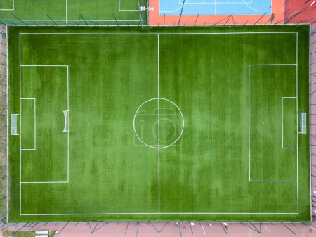 Téléchargez les photos : Vue aérienne d'un terrain de football vert luxuriant, qui semble bien entretenu et idéal pour la compétition sportive. Les marques, les poteaux de but et les gradins sont visibles d'en haut. - en image libre de droit