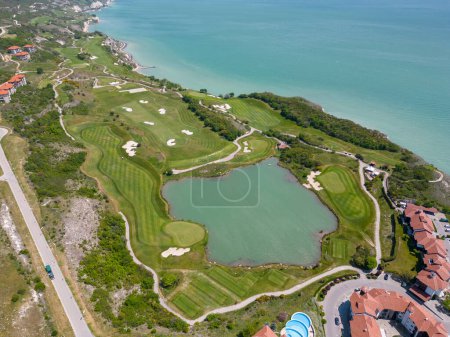 Photo for Aerial view of the golf course stretches out beneath, its lush green fairways complementing the breathtaking coastal panorama. Among the picturesque landscape, luxurious villas are strategically placed, offering a seamless fusion of elegance and scen - Royalty Free Image