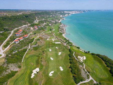 Photo for Aerial view of the golf course stretches out beneath, its lush green fairways complementing the breathtaking coastal panorama. Among the picturesque landscape, luxurious villas are strategically placed, offering a seamless fusion of elegance and scen - Royalty Free Image