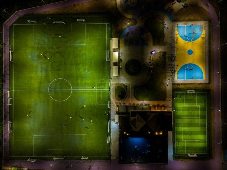 Foto de Vista aérea de un campo de deportes nocturno con campos de fútbol y baloncesto, donde los niños practican fútbol y baloncesto. - Imagen libre de derechos