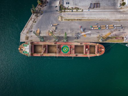 Photo for Aerial top view of a bustling seaport, where a massive cargo ship, a bulk carrier, is being loaded with wheat grains - Royalty Free Image
