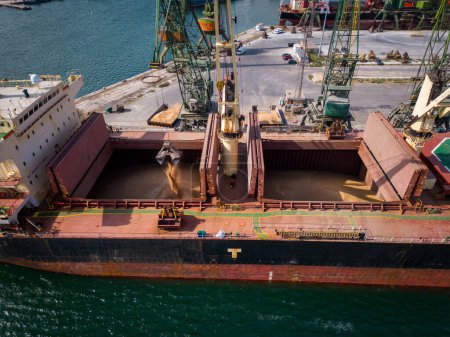 Vista aérea de primer plano de un bullicioso puerto marítimo, donde un enorme buque de carga, un granelero, está siendo cargado con granos de trigo