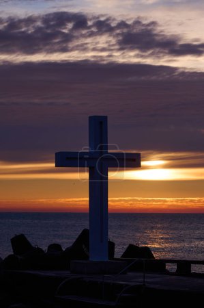 Téléchargez les photos : Croix chrétienne tôt le matin au lever du soleil. La grande croix se dresse au bord d'un brise-lames sur la côte de la mer. - en image libre de droit