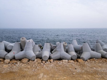 A row of concrete cylinders placed on a sandy beach.