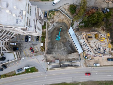 Ein Bulldozer gräbt mitten in der Stadt eine Grube für den Bau eines weiteren Gebäudes, Luftaufnahme.