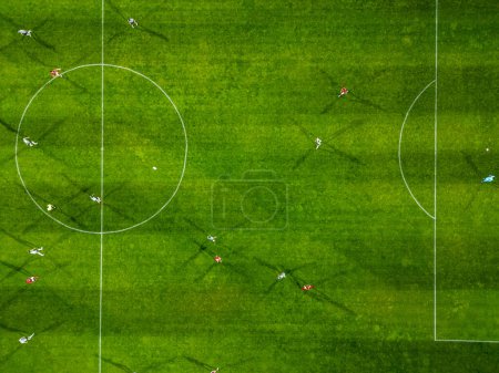 Vue aérienne d'un terrain de soccer en action, où les joueurs courent, passent et marquent des buts