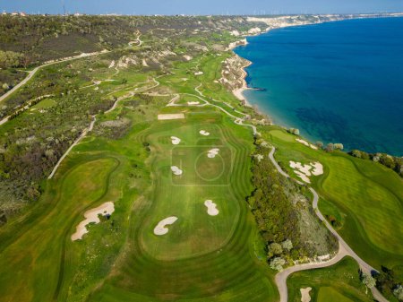 Foto de Una perspectiva aérea de un campo de golf con verdes exuberantes cerca del océano, mostrando trampas de arena y peligros del agua. - Imagen libre de derechos