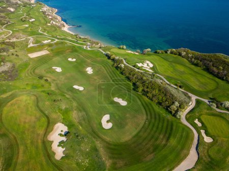 Foto de Una perspectiva aérea de un campo de golf con verdes exuberantes cerca del océano, mostrando trampas de arena y peligros del agua. - Imagen libre de derechos