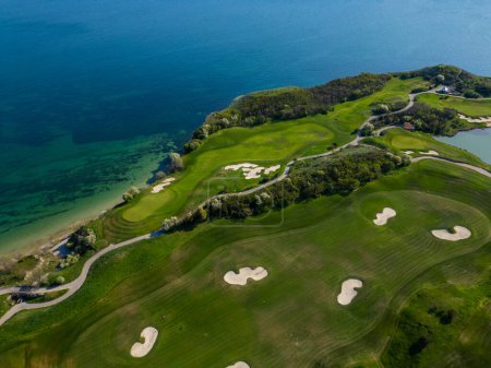Blick aus der Vogelperspektive auf einen Golfplatz in der Nähe des Ozeans mit grünen Fairways und blauem Wasser.