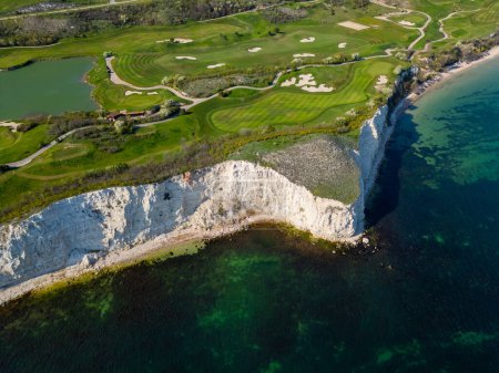 Foto de Una vista aérea de un campo de golf situado cerca del océano, mostrando calles verdes, trampas de arena y el océano azul en el fondo. - Imagen libre de derechos
