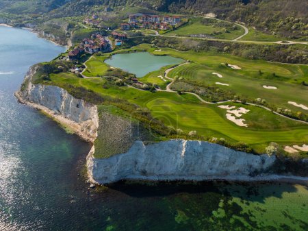 Foto de Una vista aérea de un campo de golf situado cerca del océano, mostrando calles verdes, trampas de arena y el océano azul en el fondo. - Imagen libre de derechos