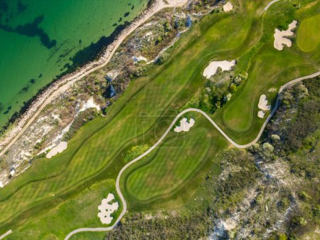 A birds eye view of a golf course located next to the ocean, showcasing the green fairways and sand traps against the backdrop of the sea.