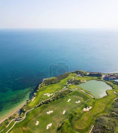 A high-angle view of a golf course set against the backdrop of the ocean, showcasing lush green fairways and sand traps.