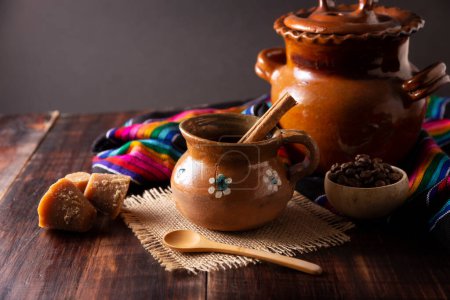 Authentischer hausgemachter mexikanischer Kaffee (cafe de olla), serviert in einem traditionellen, handgemachten Tonbecher (Jarrito de barro) auf einem rustikalen Holztisch.