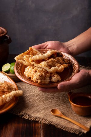 Photo for Chicharron. Crispy Fried pork rind, are pieces of aired and fried pork skin, traditional Mexican ingredient or snack served with lime juice and red hot sauce. - Royalty Free Image