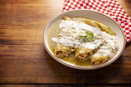 Enchiladas verdes. Plato típico mexicano hecho con una tortilla de maíz doblada o enrollada llena de pollo rallado y cubierta con salsa verde picante, crema, queso rallado y cebolla..