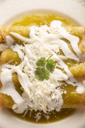 Enchiladas verdes. Plato típico mexicano hecho con una tortilla de maíz doblada o enrollada llena de pollo rallado y cubierta con salsa verde picante, crema, queso rallado y cebolla..
