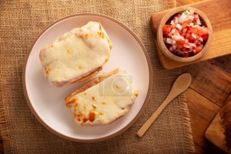 Photo for Molletes. Mexican recipe based on bolillo bread split lengthwise, spread with refried beans and gratin cheese, adding pico de gallo sauce and some protein such as ham, bacon or chorizo. - Royalty Free Image