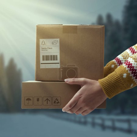 Woman holding delivery boxes for Santa Claus and wintry landscape in the background, Christmas and holidays concept