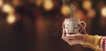 Frau mit leckerer heißer Schokolade in der Tasse und Weihnachtsbeleuchtung im Hintergrund